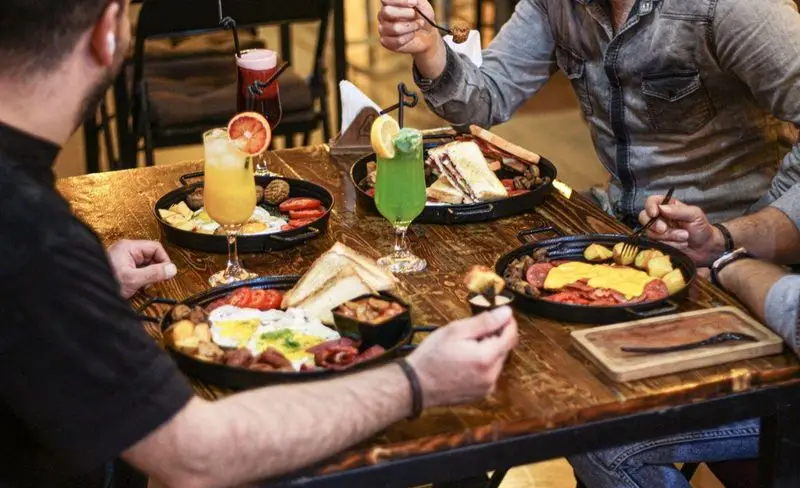 تصویری از دورهمی دوستانه در کافه فست فود برج برگر، لذت بردن از منوی صبحانه و ناهار خوشمزه با بشقاب‌های متنوع و نوشیدنی‌های تازه.