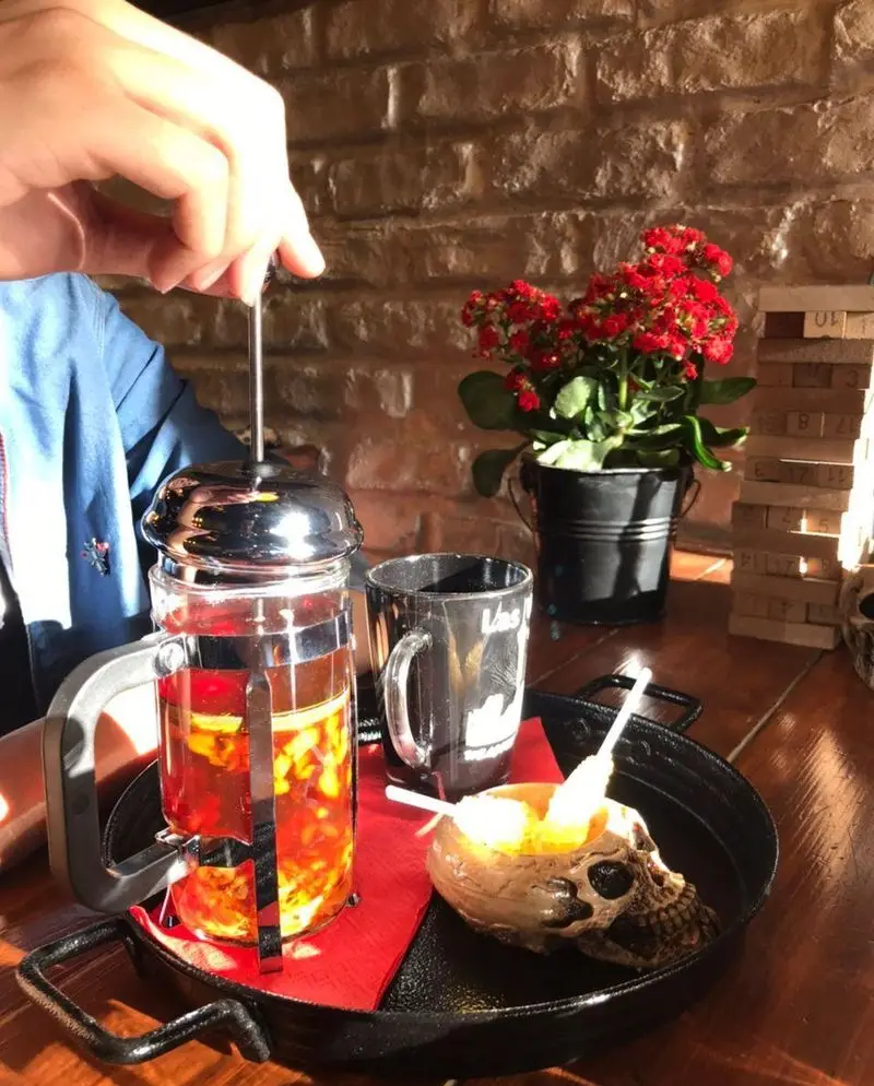 لذت نوشیدن دمنوش تازه در فرنچ پرس روی میز کافه فست فود برج برگر، به همراه لیوان و ظرف جمجمه، فضایی دلنشین و خاص.