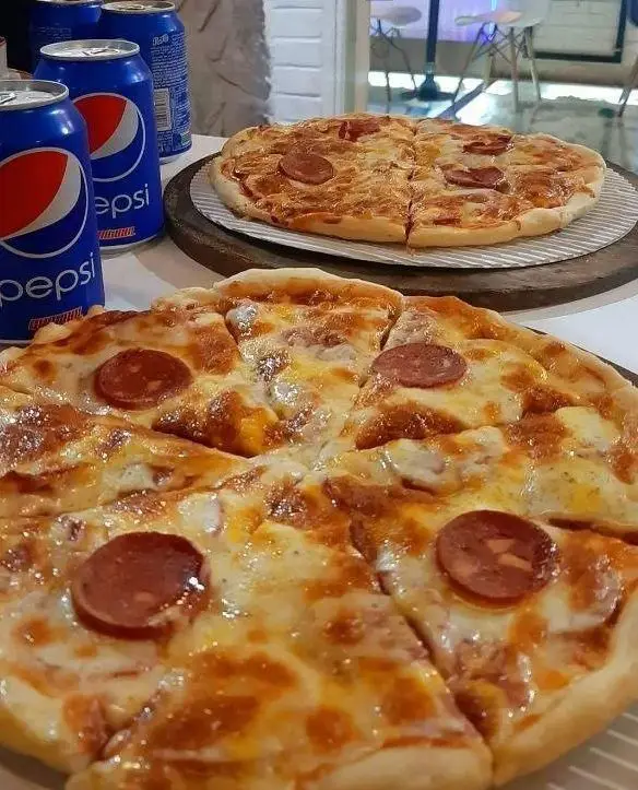 دو پیتزا پپرونی داغ و لذیذ با پنیر فراوان به همراه قوطی‌های پپسی خنک در محیط دلنشین کافه رستوران آکوا.
