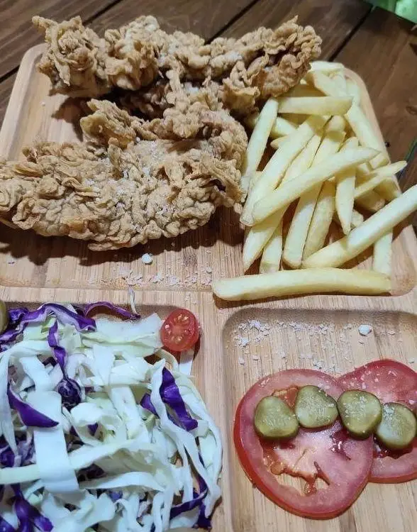 غذای خوشمزه کافه رستوران آکوا شامل فیله سوخاری ترد، سیب‌زمینی سرخ کرده، سالاد کلم تازه و مخلفات روی سینی چوبی زیبا.