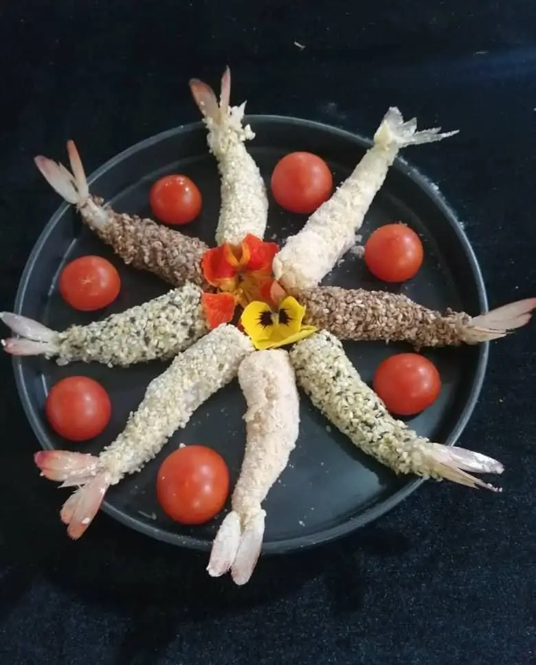 فینگر فود گرم میگو سوخاری کنجدی مجلل، آماده پذیرایی مهمانی‌ها و رویدادها. غذای دریایی شیک و لذیذ با گوجه و گل‌های خوراکی.