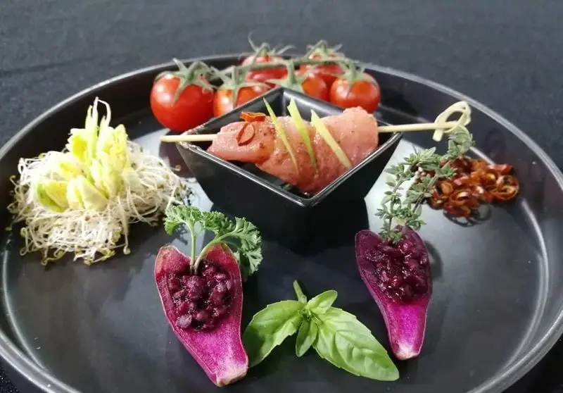 تصویری از فینگر فود گرم و مجلل: سیخ کباب، گوجه گیلاسی، جوانه، و مزه‌های بنفش پر شده. ایده آل برای کترینگ و مهمانی‌های شما.