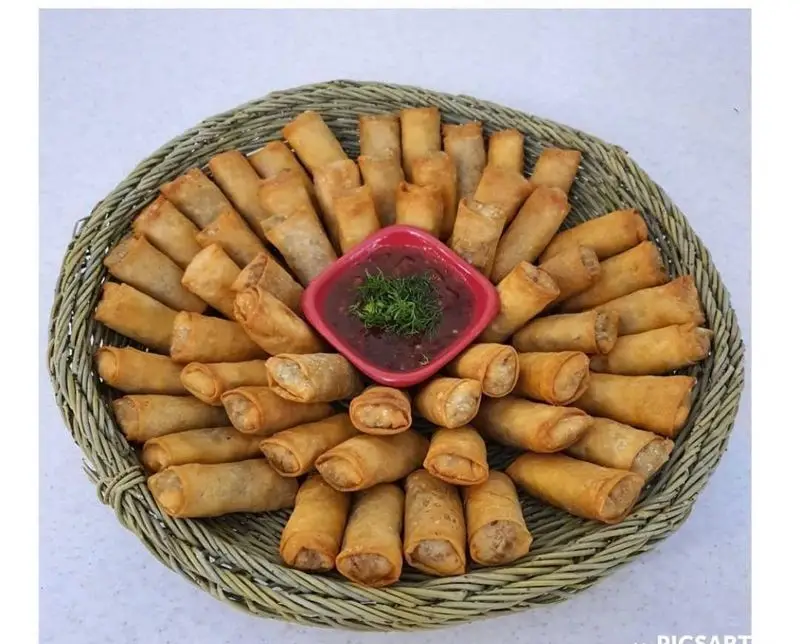 فینگر فود گرم: سینی جذاب اسپرینگ رول‌های طلایی و ترد، چیده شده در سبد حصیری با سس مخصوص. مناسب مهمانی و پذیرایی.