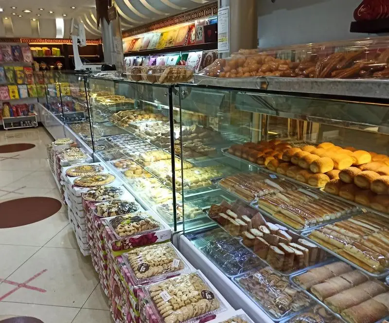 تصویری از قنادی ناتلی، ویترین‌های شیک و مدرن پر از انواع شیرینی‌های سنتی و مدرن، نان‌های شیرین، باقلوا و دسرها. کیفیت برتر.