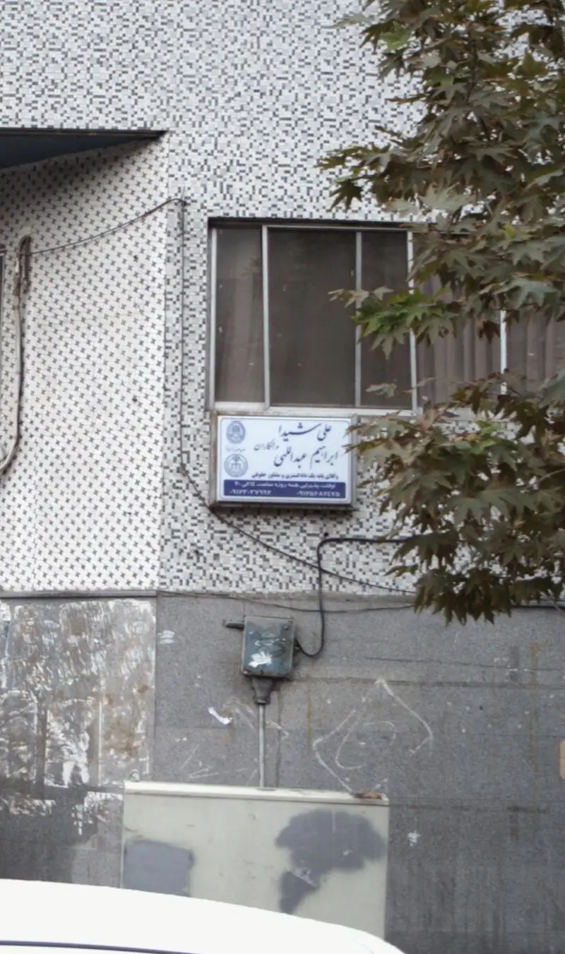 نمای ساختمان کاشی‌کاری شده در شهر، با پنجره و درختان سبز. مکانی مناسب برای کسب و کار شیرینی و خشکبار دی در محیطی آرام و در دسترس.