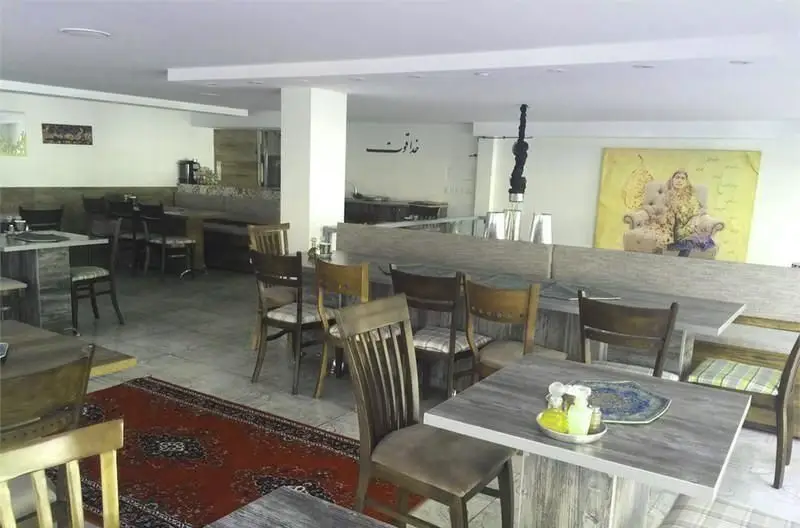 فضای داخلی دلنشین کافه رستوران شاهی با چیدمان شیک میز و صندلی‌های چوبی، نیمکت‌های راحت و فرش سنتی ایرانی، محیطی آرامبخش برای مشتریان.