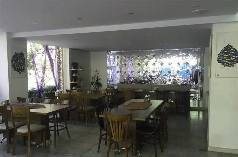 فضای داخلی کافه رستوران شاهی با میز و صندلی های چوبی شیک، دکوراسیون مدرن، پنجره بزرگ با نور طبیعی و تابلوهای هنری جذاب.