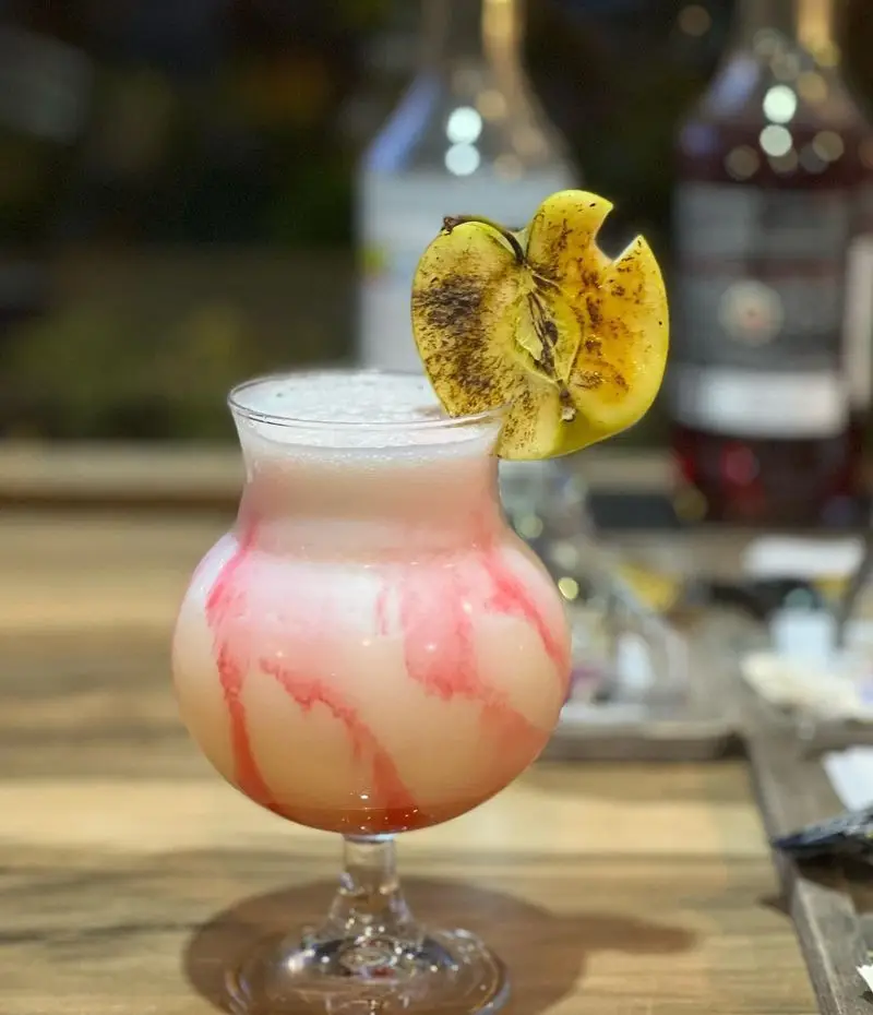 کوکتل صورتی و خامه‌ای کافه رستوران گجا با رگه‌های شربت قرمز و تزئین سیب گریل شده، نوشیدنی خوشمزه و خاص.