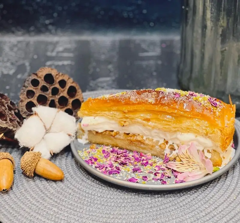 لذت طعم بی‌نظیر باقلوای کره‌ای و خامه ای با تزئین پسته و گل رز در کافه رستوران گجا، دسری دلپذیر و خاص.