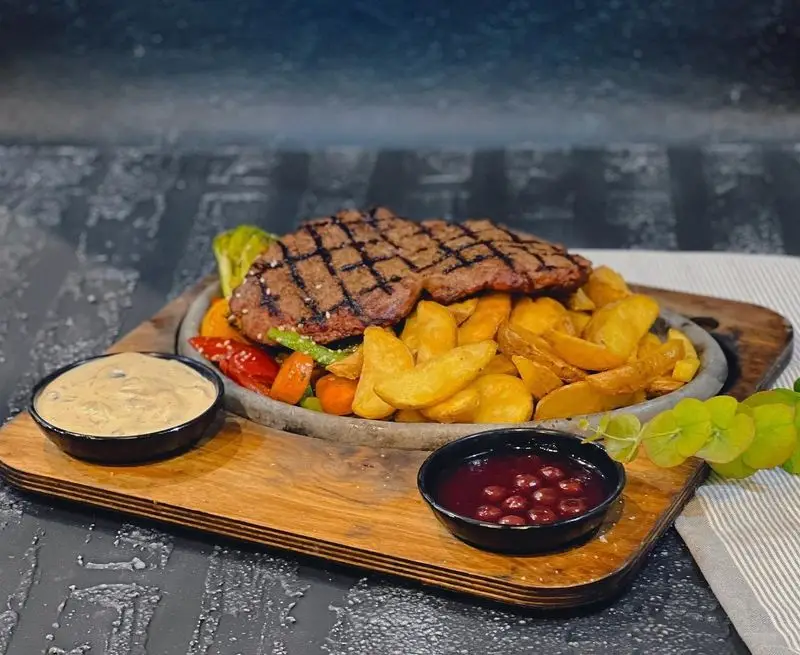 غذای اصلی: استیک گریل آبدار با دورچین سیب زمینی وجز و سبزیجات رنگارنگ تازه، سرو شده با دو سس اختصاصی در کافه رستوران گجا.