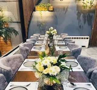 کافه رستوران گجا: فضای داخلی مدرن و دلنشین با میز غذاخوری بلند، صندلی‌های مخملی طوسی و گل‌آرایی زیبا برای تجربه‌ای به یادماندنی.