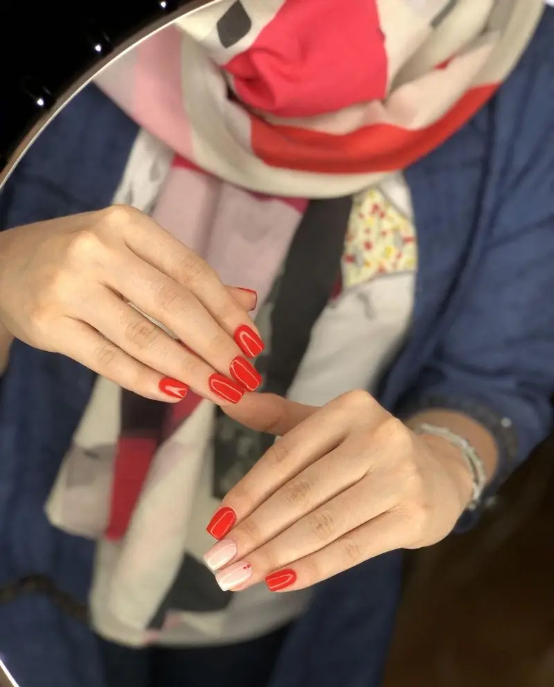 طراحی و کاشت ناخن شیک با لاک قرمز جذاب و یک ناخن با رنگ نود ملایم، مناسب برای ایده مانیکور و ژلیش ناخن در سالن زیبایی