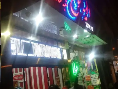 نمای جذاب و روشن فست فود الویه شوخ در شب، با تابلوهای نئونی رنگارنگ و ورودی دعوت‌کننده برای مشتریان علاقه‌مند به غذا.
