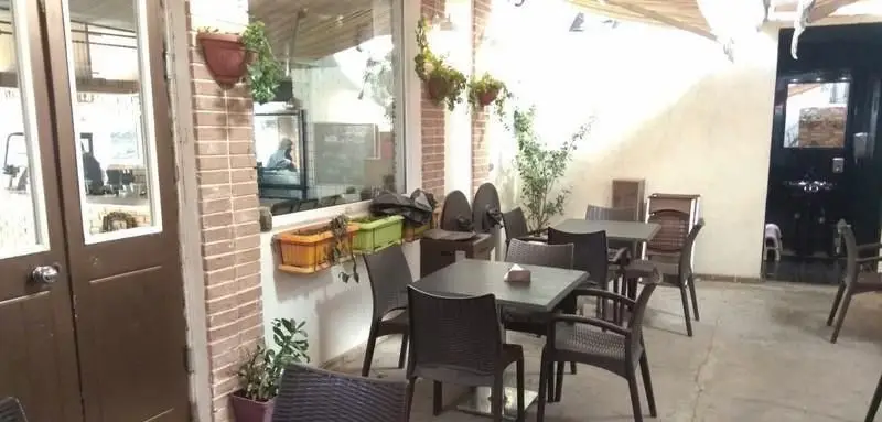 فضای نشیمن بیرونی و دلنشین کافی شاپ آلوارس با میز و صندلی‌های قهوه‌ای و گلدان‌های آویز، محیطی آرام برای مشتریان.