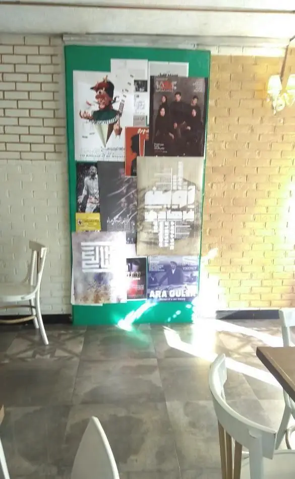 فضای داخلی دنج و هنری کافی شاپ آلوارس با دیوار آجری، صندلی‌های سفید، پوسترها و نورپردازی طبیعی، محیطی ایده‌آل برای استراحت.