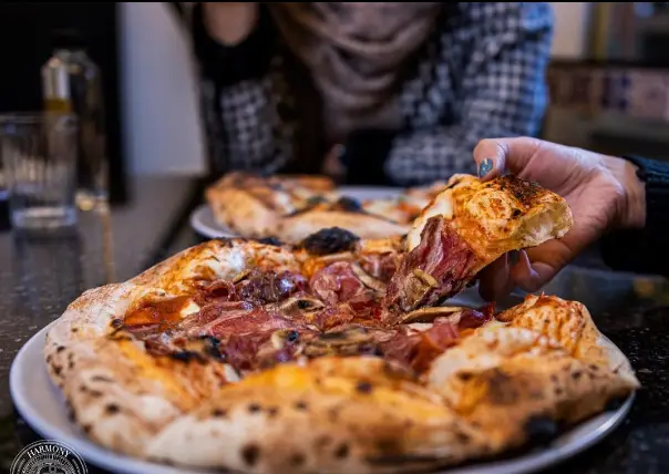 یک برش پیتزای خوش‌طعم و تازه از آشپزخانه هارمونی، با نان ترد و مخلفات لذیذ گوشت و قارچ، در دست مشتری. لذت تجربه بهترین پیتزا.