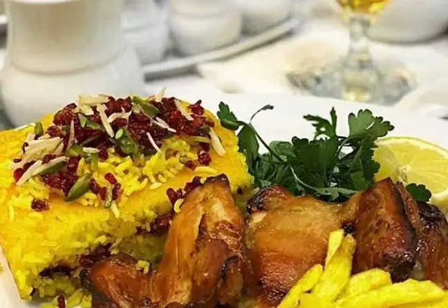 یک بشقاب غذای ایرانی لذیذ از رستوران اسلیمی: پلو زعفرانی با زرشک، پسته و بادام، در کنار تکه‌های مرغ بریان، سیب‌زمینی و لیمو تازه.