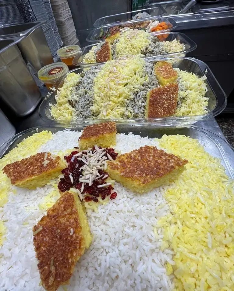کترینگ پارسی: چند سینی بزرگ غذای ایرانی شامل پلو زعفرانی، شوید پلو، ته دیگ طلایی، زرشک و خلال بادام برای پذیرایی.