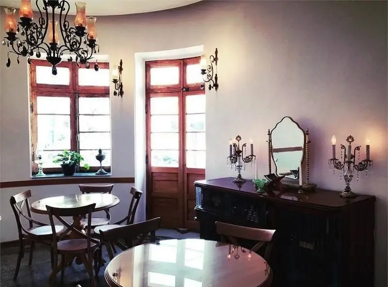 فضای دنج و کلاسیک خانه فرهنگ ماه با میز و صندلی‌های چوبی، لوستر زیبا و پنجره‌های بلند. ایده‌آل برای کافه و محافل فرهنگی.