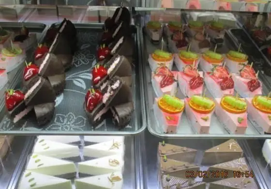 ویترین جذاب شیرینی پدیده شرق: کیک‌های شکلاتی با مغز صورتی و توت‌فرنگی، کیک‌های میوه‌ای رنگارنگ، و انواع چیزکیک و موس با تزیینات خاص.