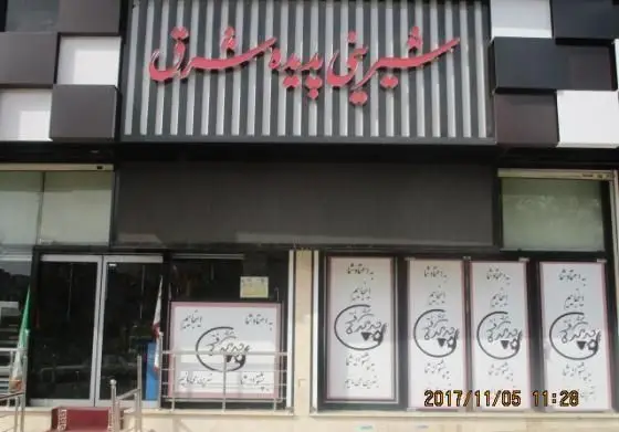 تصویری از نمای بیرونی و سردر جذاب شیرینی پدیده شرق، قنادی و شیرینی فروشی با تابلو قرمز رنگ، معماری مدرن و شیک ساختمان فروشگاه.