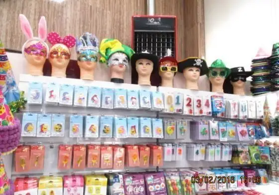 ویترین لوازم جشن و تولد با کلاه‌ها، ماسک‌های متنوع و شمع‌های عددی و فانتزی، مناسب مهمانی‌های شاد در شیرینی پدیده شرق.