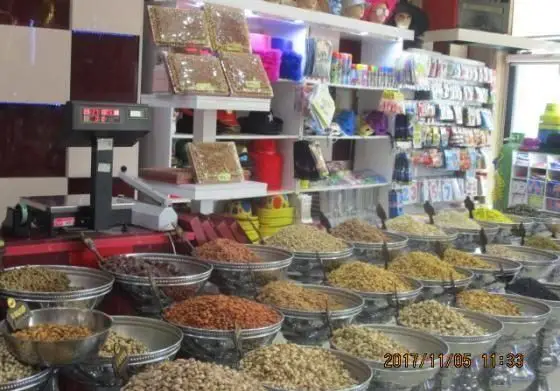 نمای داخلی فروشگاه شیرینی پدیده شرق با ردیف‌هایی از آجیل و خشکبار تازه در ظروف بزرگ، همراه با قفسه‌های محصولات بسته‌بندی و ترازوی دیجیتال.