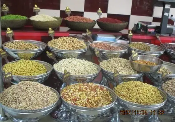 نمایش جذاب انواع آجیل، خشکبار، نخودچی و مغزها در ظروف نقره‌ای فروشگاه شیرینی پدیده شرق با قیمت‌های مشخص.