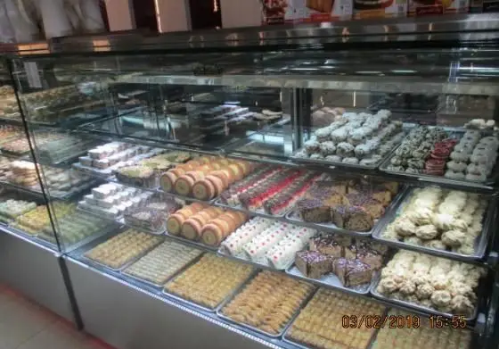 ویترین پر زرق و برق شیرینی پدیده شرق، نمایشگر چیدمان منظم و هنرمندانه انواع شیرینی خشک، باقلوا، کیک و رولت‌های تازه قنادی با کیفیت ممتاز.