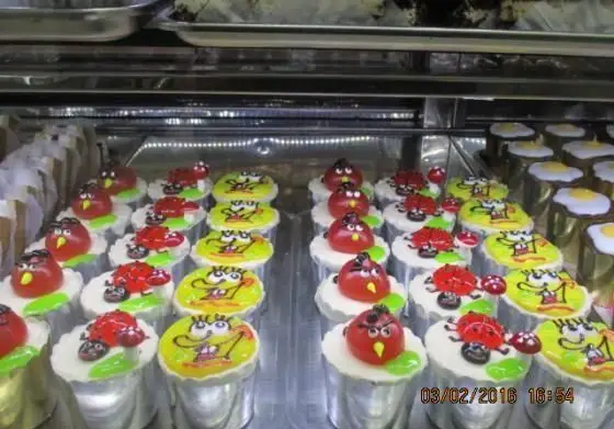 ویترین شیرینی پدیده شرق پر از کاپ کیک‌های متنوع و جذاب با تزئینات شخصیت‌های محبوب: انگری بردز، باب اسفنجی و کفشدوزک.