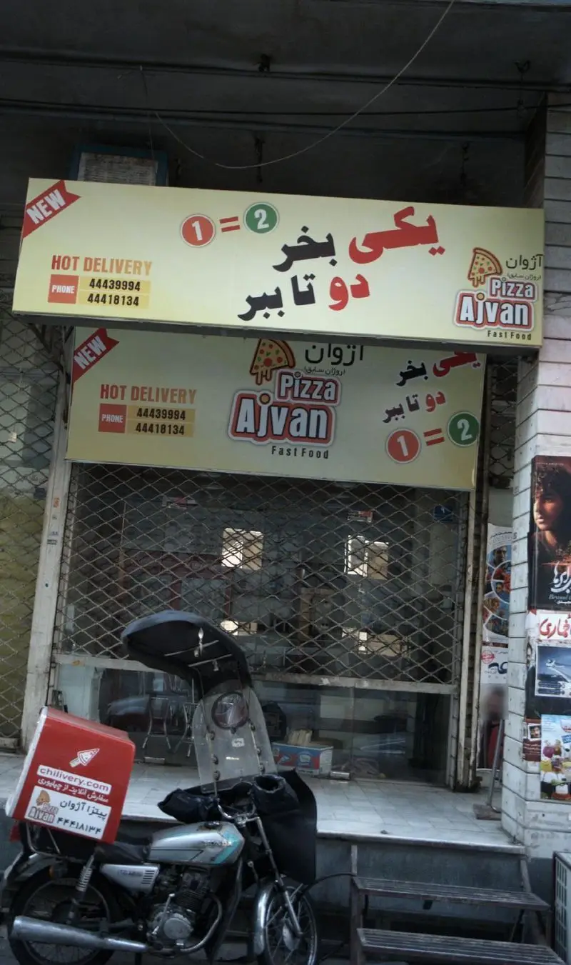 پیتزا اژوان: فست فود و پیتزا با تخفیف "یکی بخر، دو تا ببر" و خدمات ارسال سریع. شماره تماس دلیوری و موتور چیلیوری در جلوی فروشگاه.