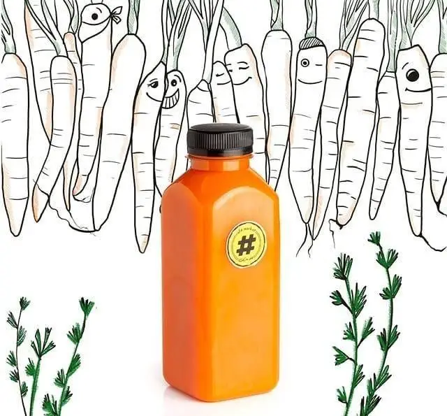 بطری آب هویج طبیعی و تازه کافه مارکت در کنار هویج های کارتونی با مزه و برگ های سبز، مناسب برای یک نوشیدنی سالم.