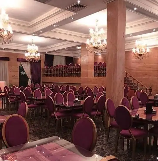 سالن مجلل و بزرگ رستوران چلو کباب جهان مهر: دکوراسیون شیک، صندلی‌های بنفش مخملی، میزهای چوبی تیره، لوسترهای کریستالی و دیوارهای مرمرین.