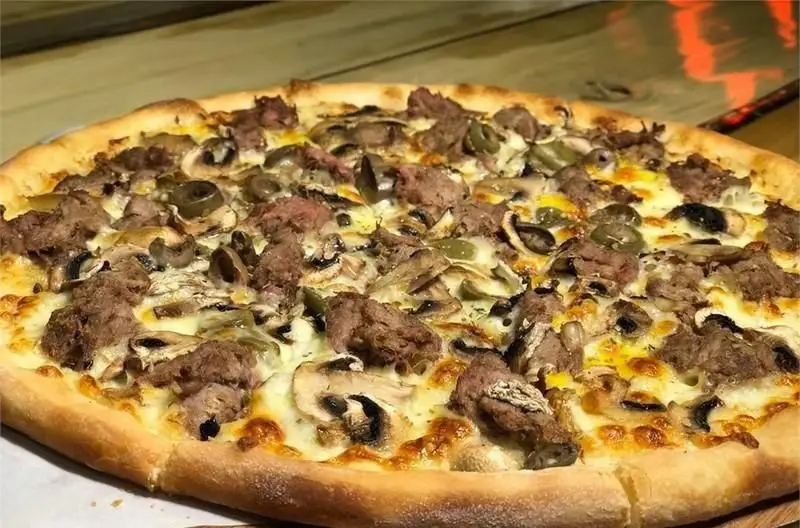 تصویری نزدیک از پیتزای گوشت و قارچ کافی شاپ اچ اند اچ با پنیر آب شده و لبه‌های طلایی، مناسب سفارش آنلاین و حضوری.