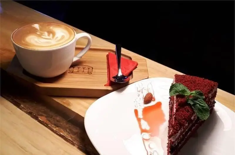 نمایی دلنشین از قهوه لاته با لاته آرت زیبا و کیک ردولوت خوشمزه در کافی شاپ اچ اند اچ، انتخابی ایده‌آل برای لذت بردن از دسر و نوشیدنی‌های ویژه.