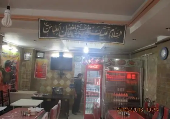 نمای داخلی رستوران آرش با چیدمان میز و صندلی، یخچال نوشیدنی و بنر مذهبی چشمگیر. محیطی سنتی و صمیمی برای لذت بردن از غذاهای اصیل ایرانی.