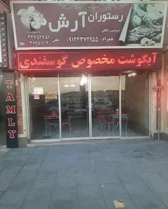 رستوران آرش با تابلوی رستوران و عکس آبگوشت گوسفندی، ورودی شیشه‌ای و فضای داخلی با میز و صندلی قرمز، آماده پذیرایی است.