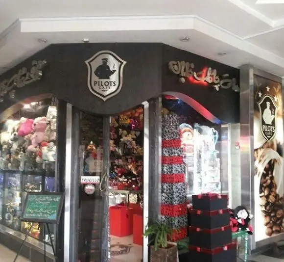 نمای بیرونی کافه خلبان Pilots Cafe با طراحی مدرن، لوگوی خلبان، ورودی تزئین شده و تابلوی کافه با قهوه.