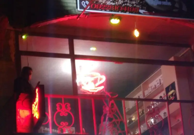 ورودی کافه رها در شب با نورپردازی قرمز و تابلوی نئون قهوه، آماده پذیرایی از شما. شماره تماس: 09228104109