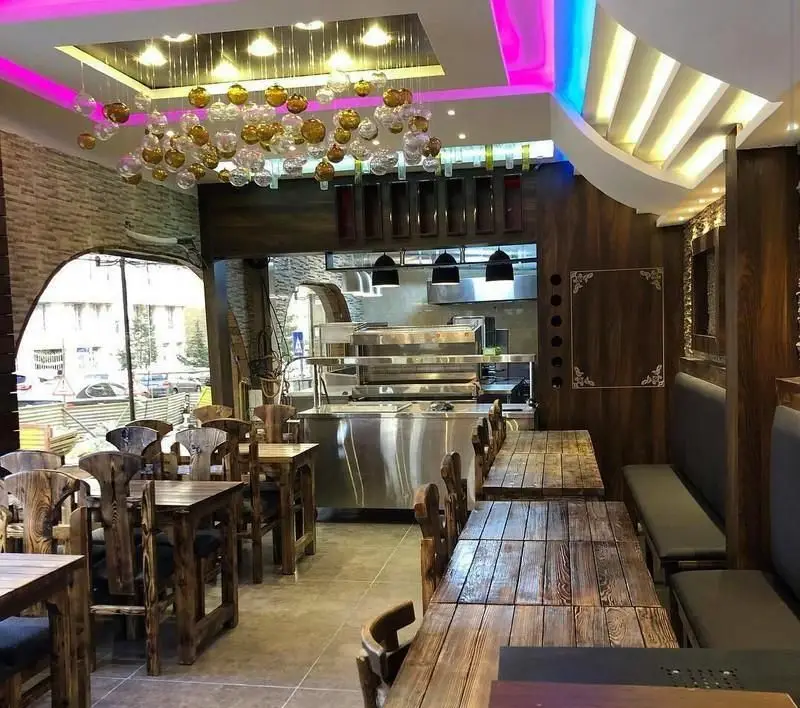 فضای داخلی شیک و مدرن فست فود سیموتو با میز و صندلی‌های چوبی، آشپزخانه مجهز و نورپردازی جذاب برای تجربه غذایی دلپذیر.