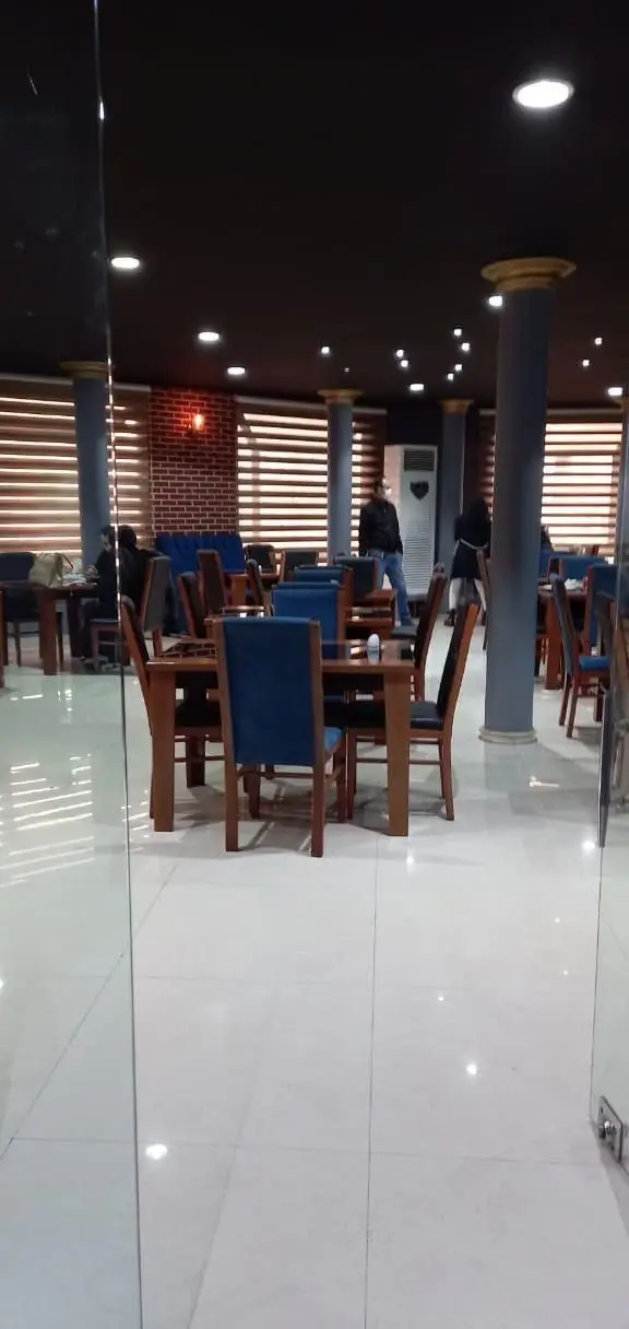 محیط داخلی رستوران شب‌های تهران، با میزهای چوبی، صندلی‌های آبی، نورپردازی مدرن و حضور مشتریان در فضایی دلپذیر.