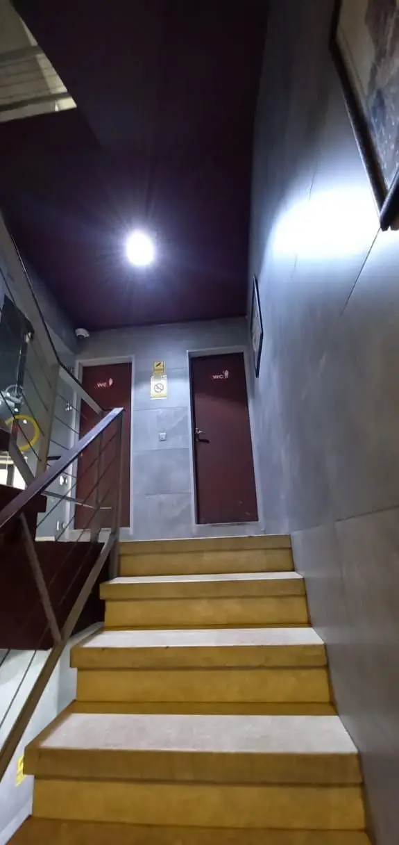 پله‌های داخلی رستوران شب‌های تهران، منتهی به سرویس‌های بهداشتی با درب‌های قهوه‌ای WC، نرده استیل و نورپردازی سقفی روشن.