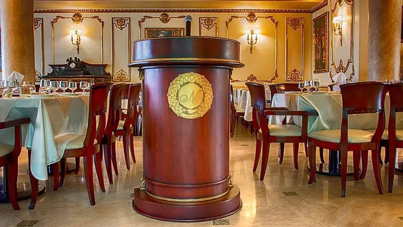 نمای داخلی شیک و مجلل رستوران نایب ساعی: میزهای چیده شده آماده سرو، صندلی‌های چوبی زیبا و جایگاه سخنرانی کلاسیک با لوگوی N.