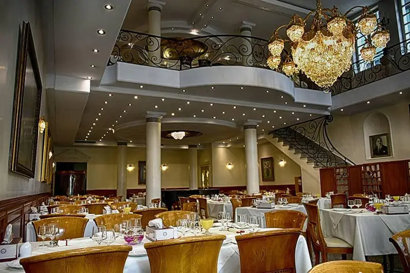 فضای داخلی لوکس و شیک رستوران نایب ساعی با چیدمان کامل میزها، لوستر کریستالی مجلل و بالکن چشم‌نواز.