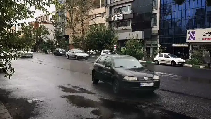 منظره‌ای از خیابان اصلی جلوی رستوران نایب ساعی، نمایش دهنده محیط شهری با آسفالت خیس و عبور خودروها در روز بارانی.