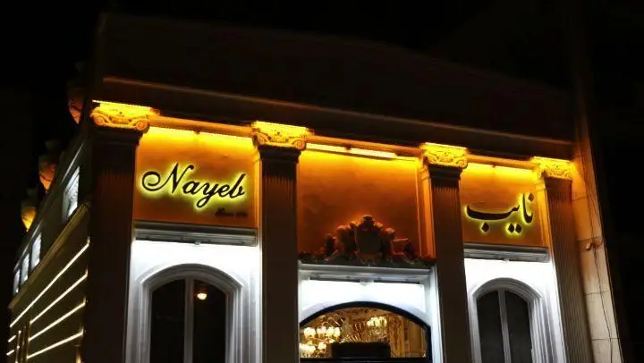 نمای شب رستوران نایب ساعی با نورپردازی زیبا و گرم، تابلوی نئونی "Nayeb" و "نایب". بهترین رستوران و کبابی ایرانی در تهران.