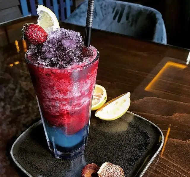 نوشیدنی اسموتی لایه‌ای قرمز، آبی و بنفش کافه رستوران ایتالیایی بلوکازا، مزین به یخ، توت فرنگی و لیمو؛ تجربه‌ای خنک و دلچسب.