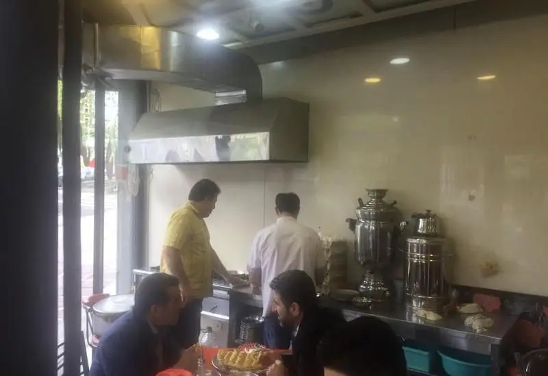رستوران ایرانی املت و دیزی سرای علی: آشپزخانه باز، کارکنان مشغول پخت و پز، سماورهای سنتی و مشتریان در حال صرف غذا.