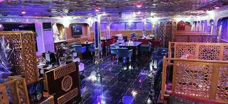 رستوران فرنگی شاخه طوبی: فضای داخلی لوکس با دکوراسیون مدرن و عناصر سنتی، نورپردازی بنفش، سقف نقوش‌دار و میز و صندلی‌های شیک.