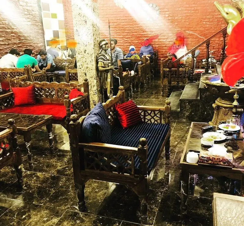 فضای گرم و دلنشین سفره خانه سنتی تگرگ با دکوراسیون چوبی زیبا، مبلمان سنتی با کوسن‌های قرمز و آبی، و مشتریان.